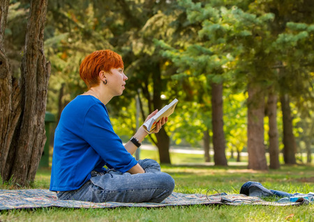 Redheaded girl reading a book on a glade in the park.の写真素材