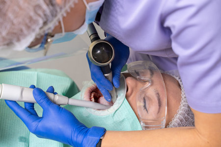 A dentist with the help of specialized tools treats caries in the oral cavity of a girl patient.