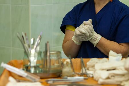 during the operation, the surgeon assistant holds his hands clasped hand in hand in front of the chest, in the foreground is a table with surgical instruments.の写真素材