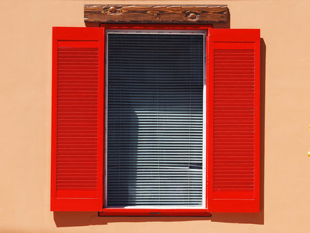 Vintage window on the wall with red shutters and white blinds closeup