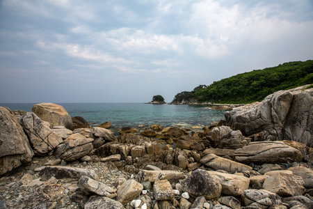 A rugged and rocky shoreline featuring a small island far in the distanceの写真素材