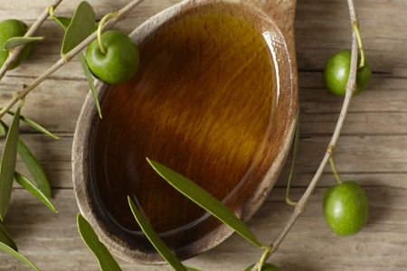 Green olive branch and a spoon full of oil on the wooden table の写真素材