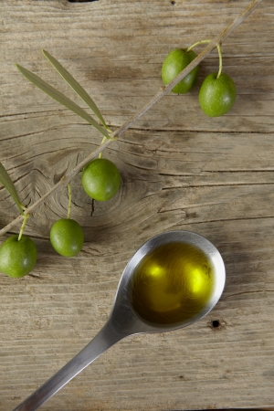 Green olive branch and a spoon full of oil on the wooden table の写真素材