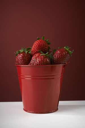 fresh red strawberries in a red bowl on checkered tablecloth, with red backgroundの写真素材