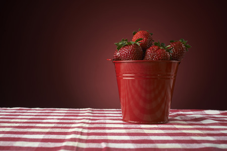 fresh red strawberries in a red bowl on checkered tablecloth, with red backgroundの写真素材