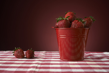 fresh red strawberries in a red bowl on checkered tablecloth, with red backgroundの写真素材