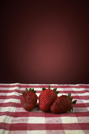 fresh red strawberries in a red bowl on checkered tablecloth, with red backgroundの写真素材