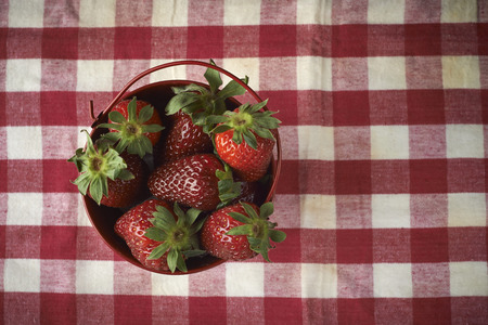 fresh red strawberries in a red bowl on checkered tablecloth, with red backgroundの写真素材