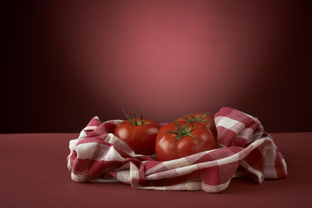 fresh red tomatoes on checkered tablecloth, with red backgroundの写真素材