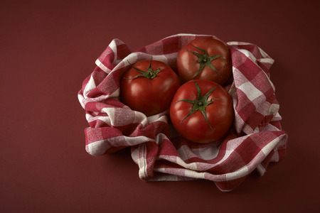 fresh red tomatoes on checkered tablecloth, with red backgroundの写真素材