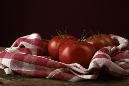 fresh red tomatoes on checkered tablecloth, with red backgroundの写真素材
