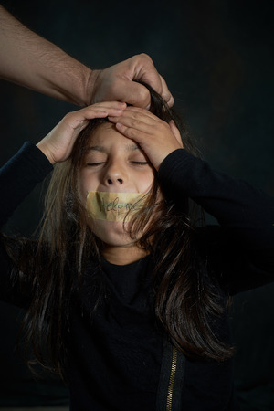 Girl cries as a guy pulls her hair while her mouth is closed with tape writing help me の写真素材