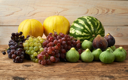 many fresh autumn fruits grape melon watermelon figs on a wooden kitchen tableの写真素材