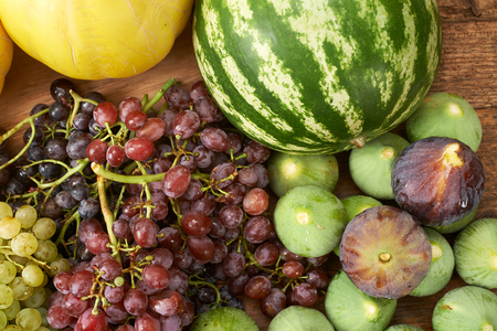 many fresh autumn fruits grape melon watermelon figs on a wooden kitchen tableの写真素材