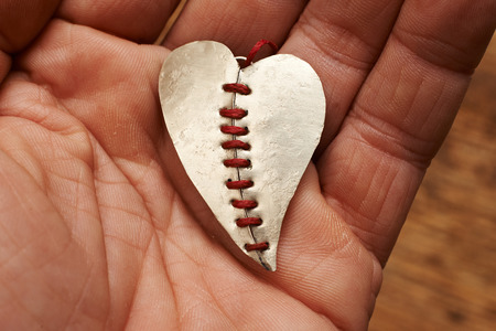 broken heart stitched with red thread on a handの写真素材