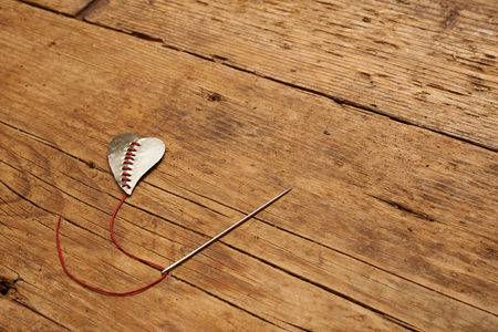 broken heart stitched with red thread on wooden table.の写真素材