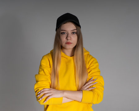 in the studio, a girl in a yellow sweatshirt and a black cap looks into the lens, the background behind her is grayの素材 [FY310166555301]