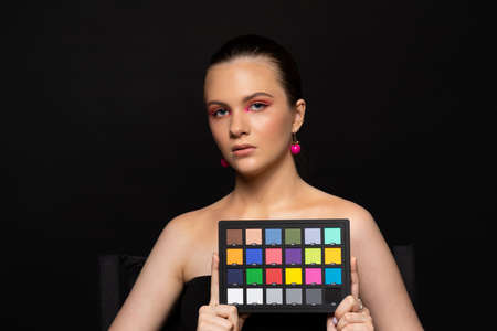 High beauty photo of a lovely young girl with blue eyes, round pink earrings and wonderful professional makeup, with long brown hair. Posing over black background. Close-up. Studio shot. Portraitの写真素材