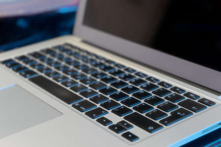 Modern slim laptop detail of keyboard, slightly tinted in blue, the entire keyboard, part of the screen and part of the touchpad are visibleの写真素材