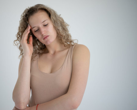 A pensive girl touches her temple with her hand, she is very sad. she is wearing a beige bodysuit....