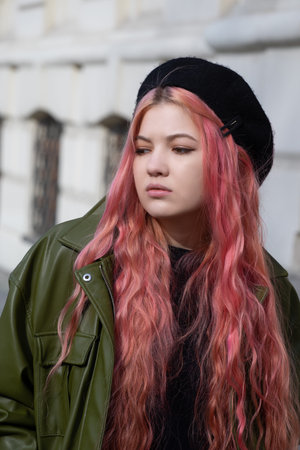 A disgruntled girl in a black beret, with long pink hair, in a green jacket, behind her is the...