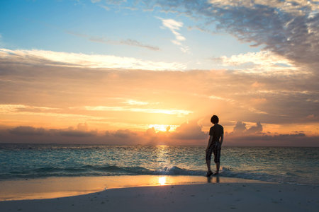 Man stands on the beach and watches the sunset