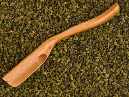 Wooden scoop over dry green tea leaves backgroundの写真素材