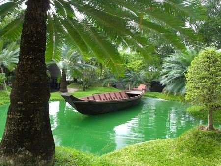 traditional wooden boat floating on the green lake surrounded with the palm trees, Thailand, SE Asiaの写真素材