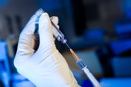 Scientist using syringe sucking vaccine, white gloves, blue backgroundの写真素材