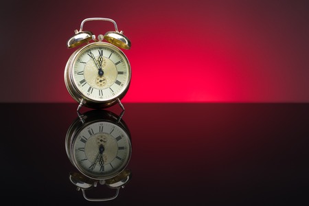 Vintage alarm clock showing five minutes to twelve, red background, copy spaceの写真素材