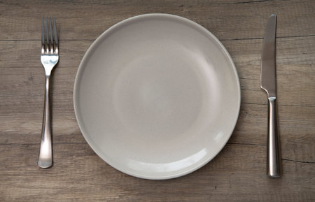 Ceramic plate, fork and knife on wooden planks table