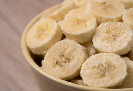 Fresh ripe organic sliced bananas in a ceramic bowl on a wooden table.の写真素材