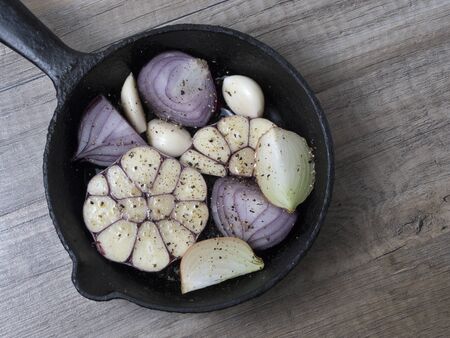Slices of garlic, red and yellow onion in a frying pan with spices, on wooden background. Top view.の写真素材