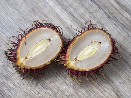 Two halves of a rambutan on a wooden background. Close up view.の写真素材
