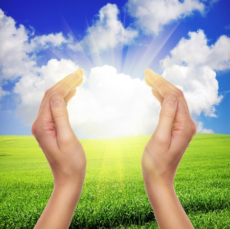female hands holding sun over green field of grass and blue sky - religion and environment conceptの写真素材