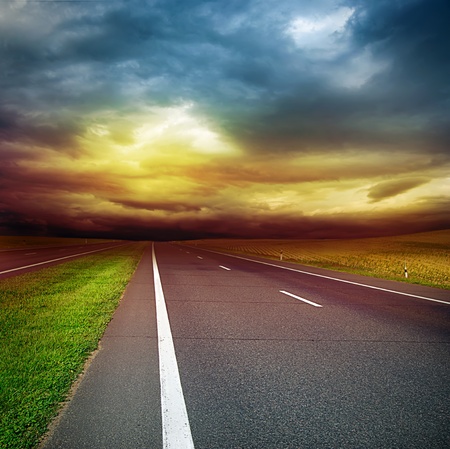 asphalt road in the field over stormy dark cloudy sky - sunset in the evening の写真素材
