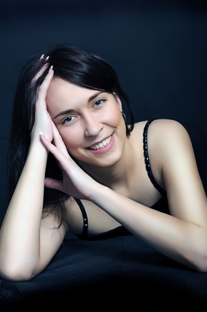 portrait of a young smiling brunette  woman with arms crossed under her hair on dark black backgroundの写真素材