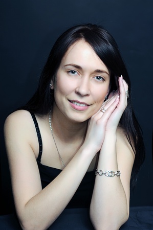 portrait of a young smiling brunette woman with arms crossed under her hair on dark black background の写真素材