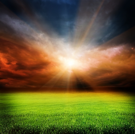 stormy evening clouds in the sky and green field of grass with sun light passing throughの写真素材