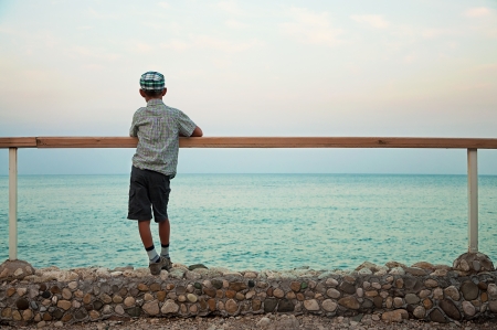 silhouette of a boy standing on quay in the evening during sunset looking at seaの写真素材