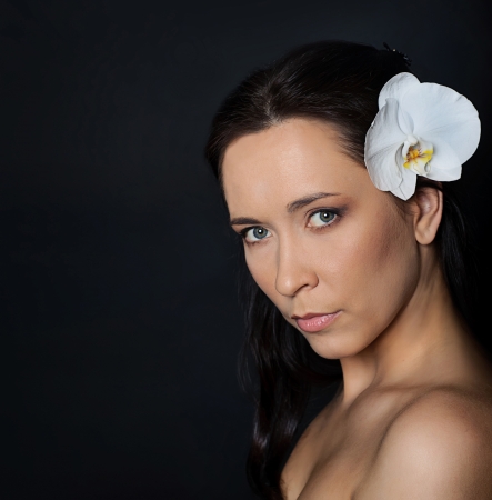  portrait of brunette woman with white orchid in hair over blackの写真素材