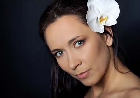 portrait of brunette woman with white orchid over black backgroundの写真素材