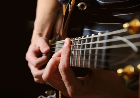 close up shot of strings and guitarist hands playing guitar over black - shallow DOF with focus on handsの写真素材