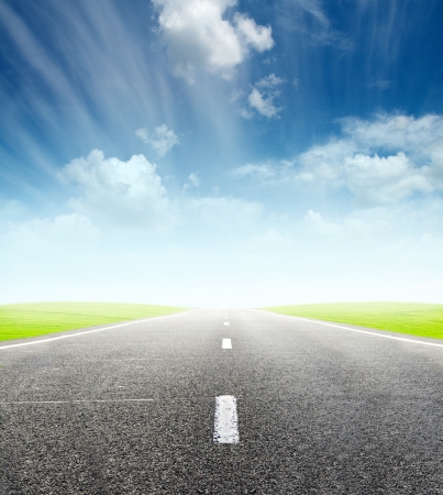 green field and road over blue cloudy sky - travel and tranportation conceptの写真素材