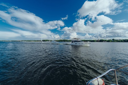 View from the board of a sailing yacht on the waters, sailing ships and the forest growing along the coast, as well as people's homes. Expanse of water reservoirs, beautiful cloud drifting over the waterの写真素材