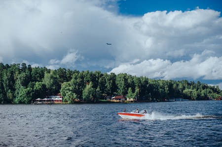 View from the board of a sailing yacht on the waters, sailing ships and the forest growing along the coast, as well as people's homes. Expanse of water reservoirs, beautiful cloud drifting over the waterの写真素材