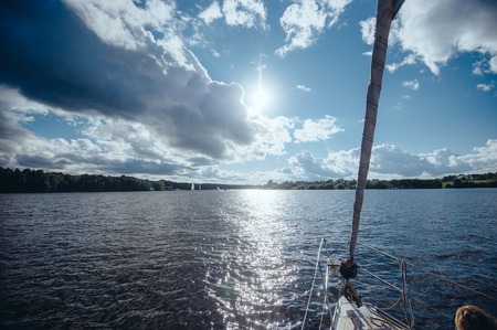 View from the board of a sailing yacht on the waters, sailing ships and the forest growing along the coast, as well as people's homes. View from the boat nose of the surrounding water spaces and the woods on the lakeの写真素材