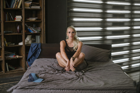 athletic woman in body poses for a photographer sitting on a double bed.の写真素材