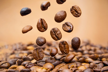 coffee beans close up falling on pile against brown background