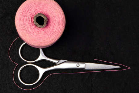 spool of pink thread and scissors on dark backgroundの写真素材